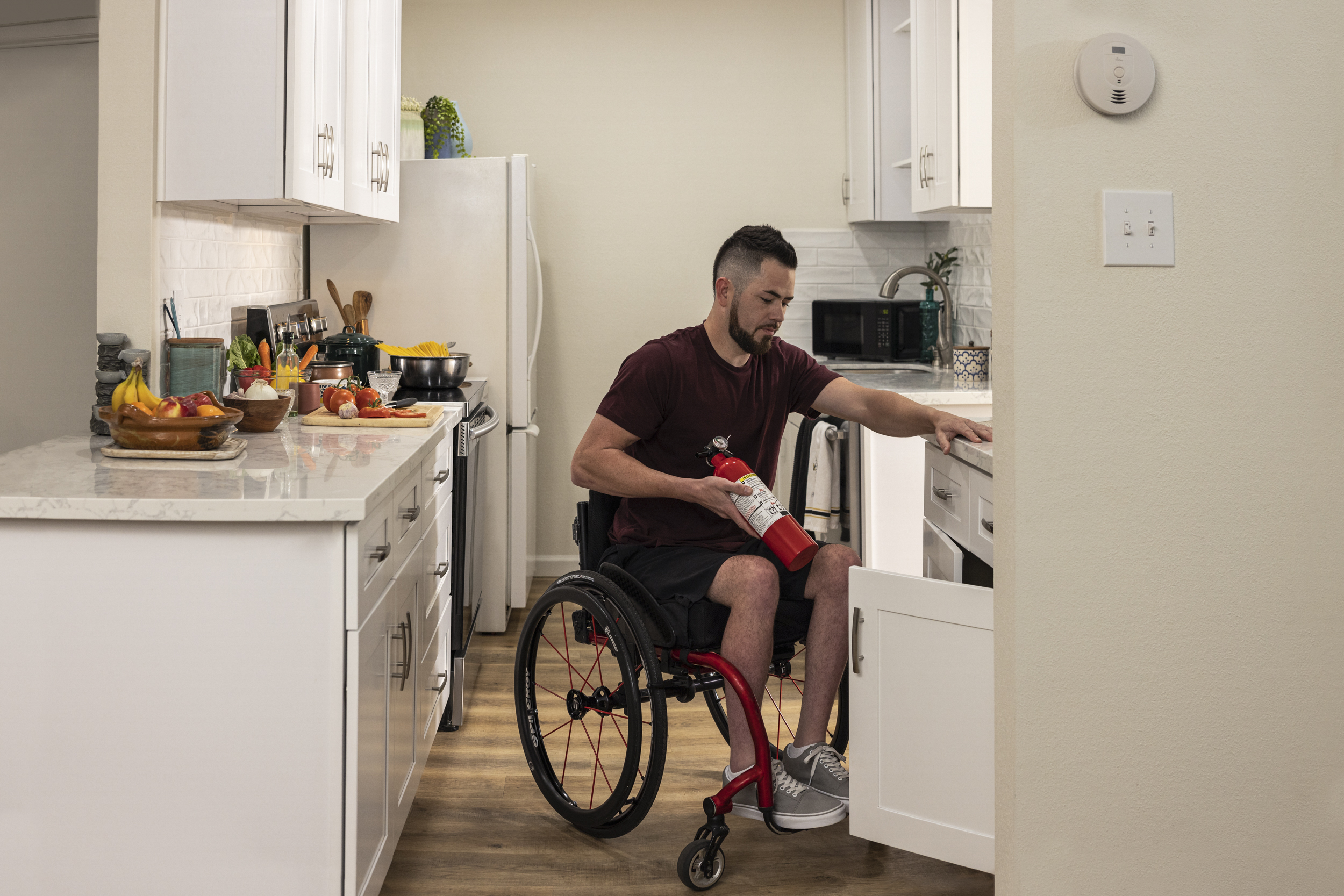 Seguridad contra incendios - persona en silla de ruedas guardando un extintor de incendios en su cocina.