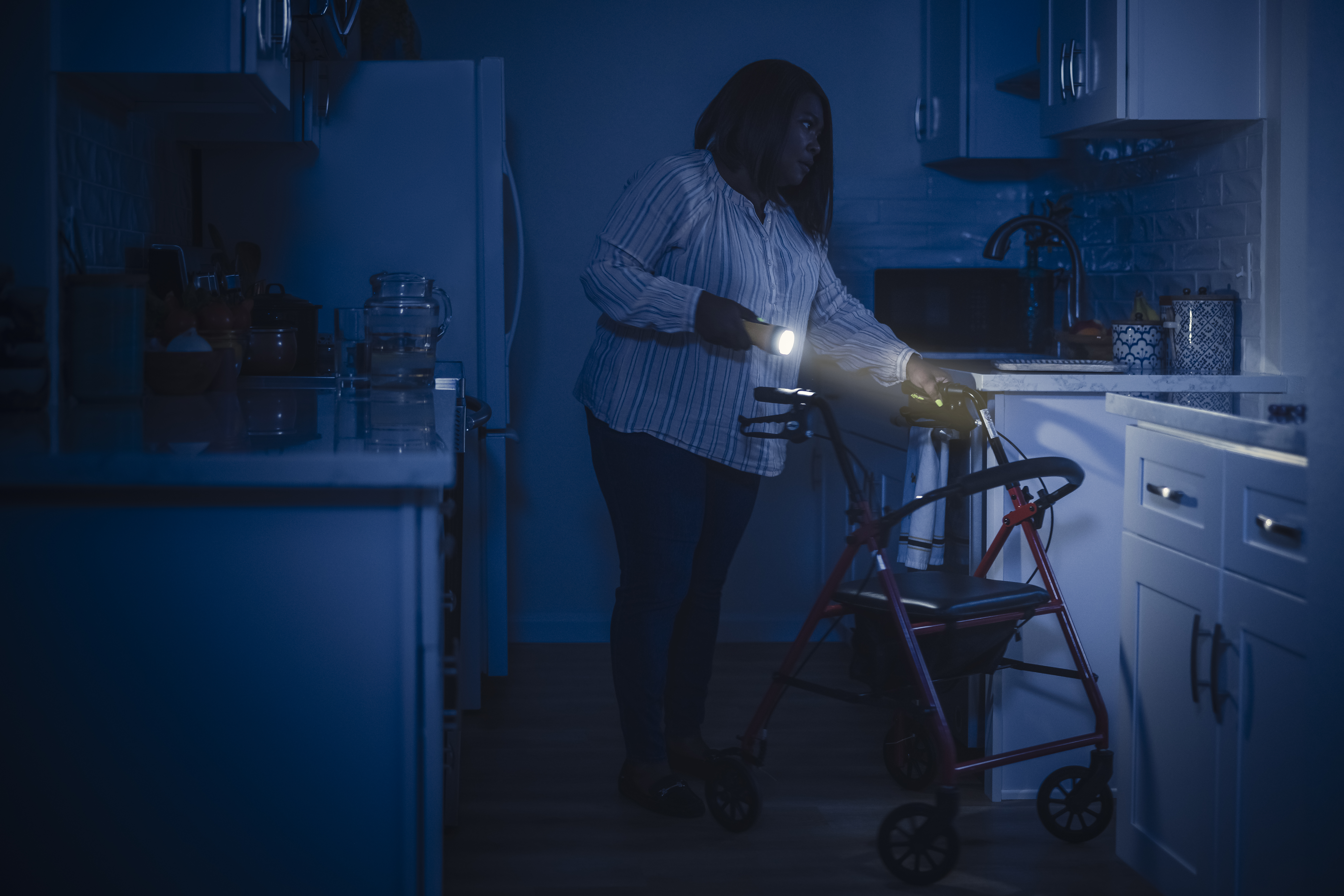 Storm Safety - Person who uses a walker using a flashlight in their kitchen during a power out.