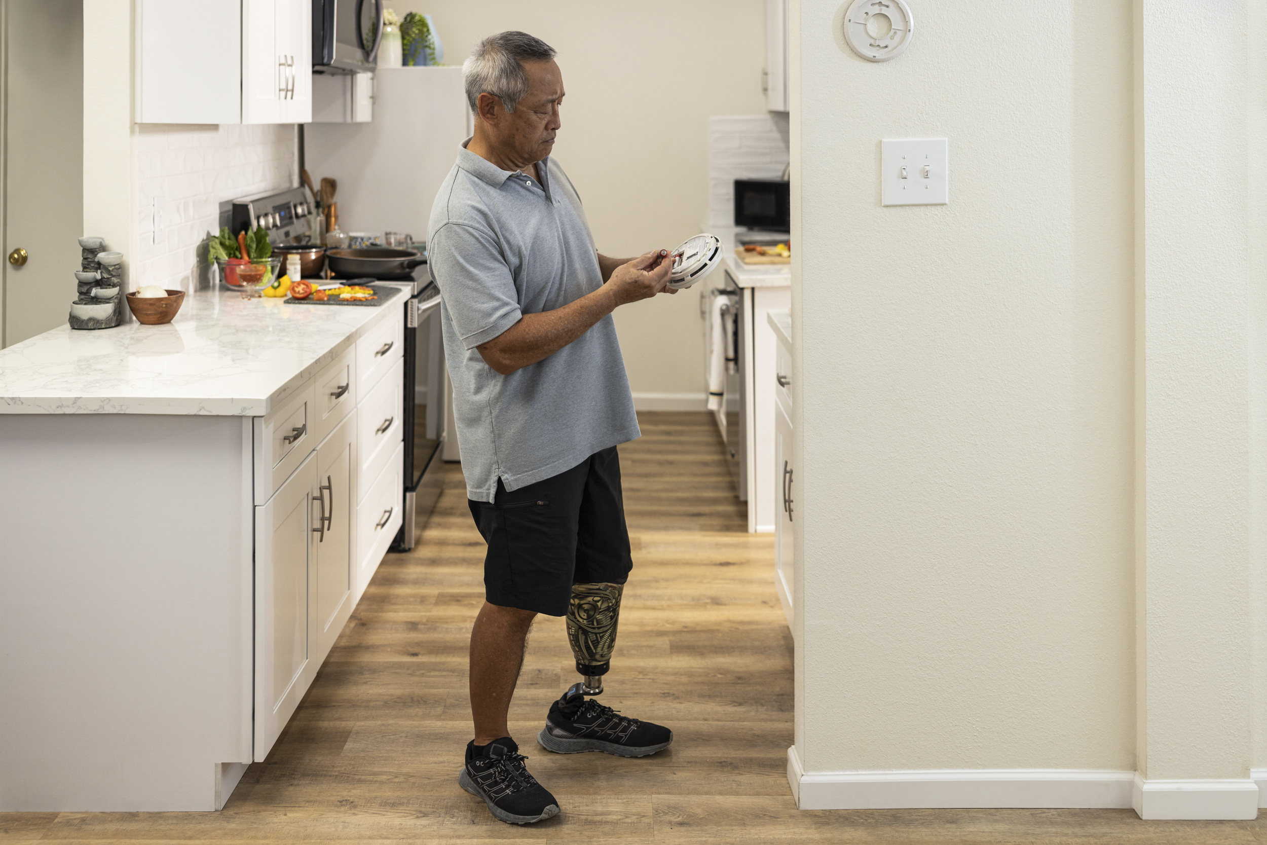 Seguridad contra incendios - Persona con una pierna prostética inspeccionando las baterías de su detector de humo.
